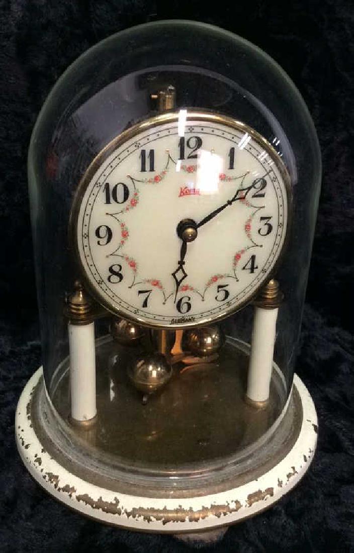 KOMA Vintage German Standing Clock: KOMA Vintage German Standing Clock. Standing analogue clock, with circular footed pedestal and glass dome cover. Pedestal is painted cream tones. Clock face is decorated with floral design. Some surfa