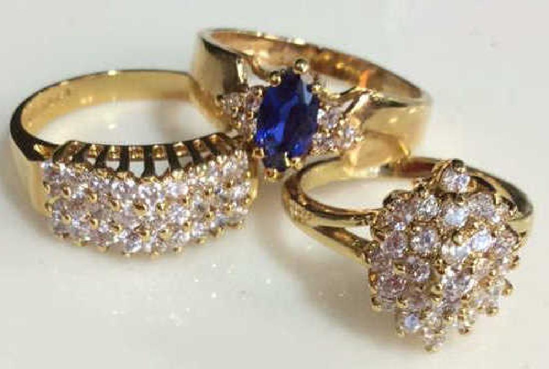 Lot 3 Rhinestone & Gold Plated Rings: Lot 3 Rhinestone & Gold Plated Rings. One ring with oval cut blue toned rhinestone framed on both sides by three round cut colorless rhinestones, marked as S 14 K HGE LIND. One unmarked ring, costume 