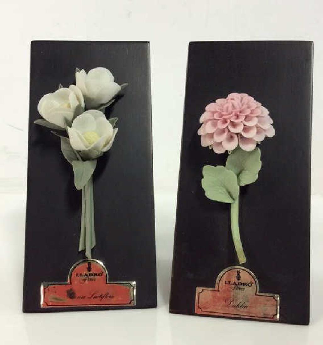 Pair LLADRÓ Vintage Sculpted Porcelain Flowers: Pair LLADRÓ Vintage Sculpted Porcelain Flowers on wooden triangular bases. Sculpted porcelain flowers mine dahlia and one paeonia lactiflora. One piece comes with original box. Measures approx 5 in t