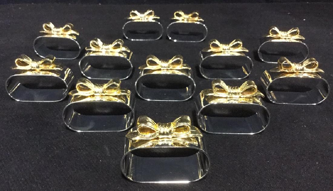 Set Of 12 Silver And Gold Metal Napkin Rings: Set Of 12 Silver And Gold Metal Possibly Plated Napkin Rings With Bow Motif. Oval shaped silver toned metal rings with gold toned metal bows mounted on top. Unused and marked on interior with stickers