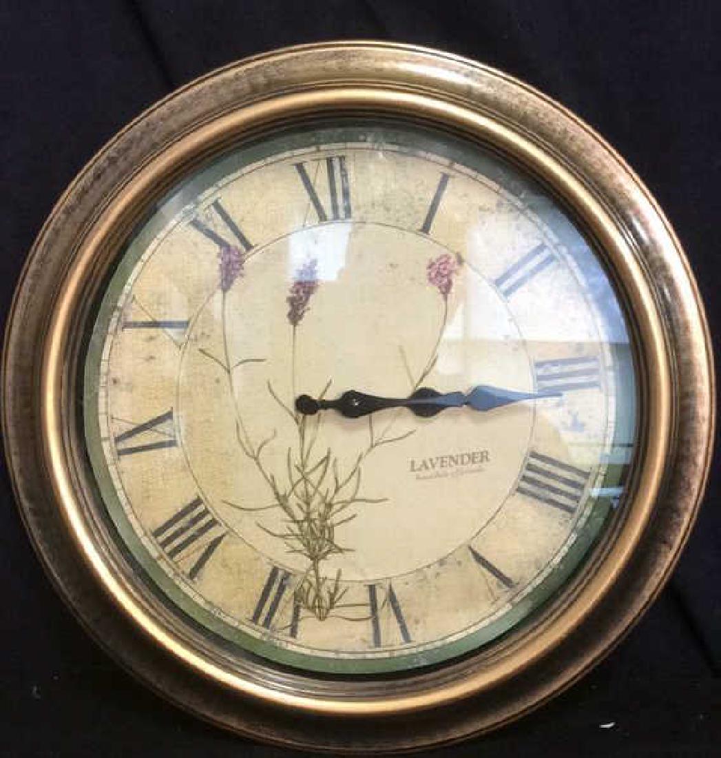 Lavender Round Wall Clock: Clock face has floral detail. Reads Lavender on right side. Contains roman numerals and black toned hands. Frame of clock is gold toned. Measures approx 16 inches diameter.