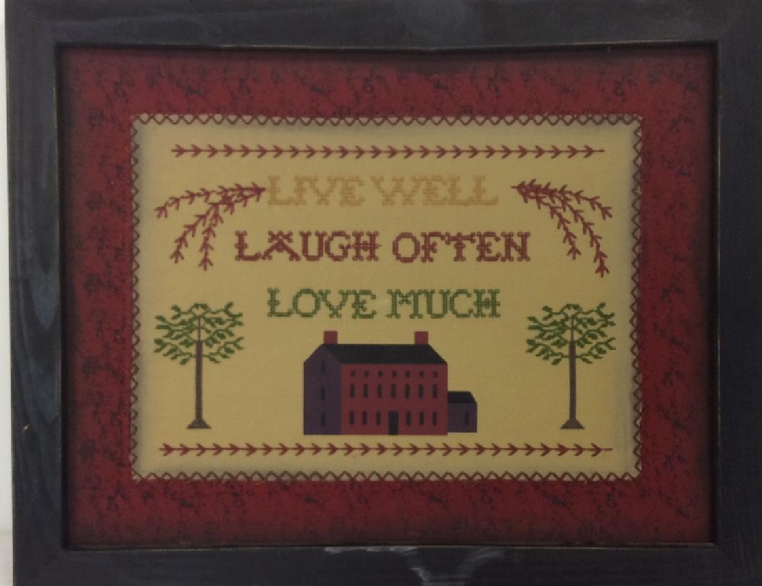 Live Well Laugh Often Love Much Embroidery: In style of Antique Sampler, possibly vintage, fabric art, needle craft art, Live Well Laugh Often Love Much embroidery on tan toned fabric with a red and black patterned matte. Fabric contains print
