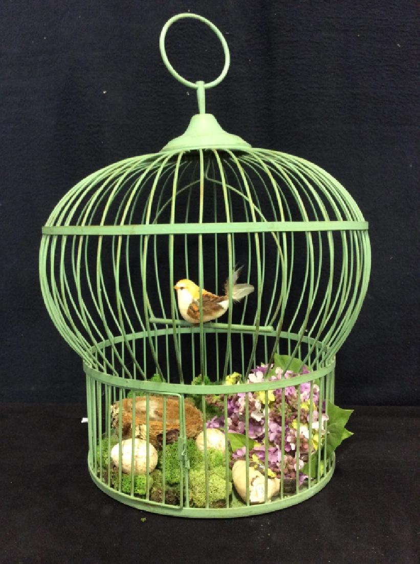 Hanging Bird Cage w/ Greenery and Bird Accessories: Bird cage is green toned metal with wooden carved birds with feather detailing. Bird cage includes wooden painted bird eggs, plastic purple and green toned flowers, and moss accents. Cage measures app