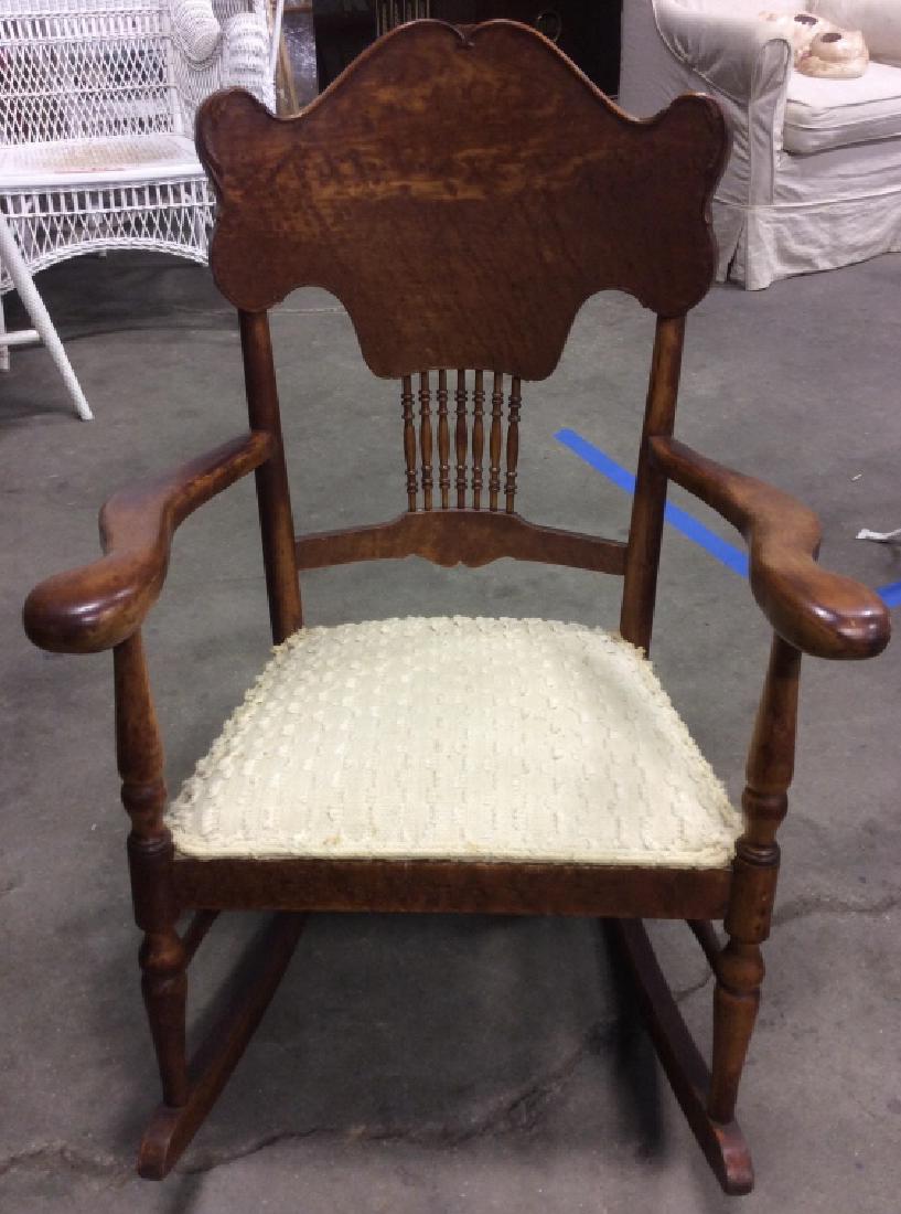 Antique Wooden Rocking Armchair: Antique wooden rocking armchair contains cream toned ruffled padded upholstery. Seating has some tears and discoloring. Measures approx 36 inches tall x 25 inches wide x 30 inches deep.