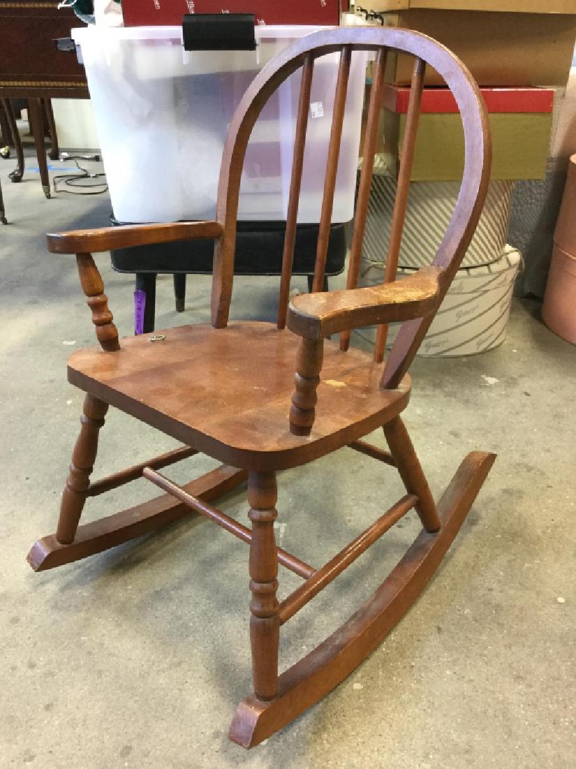 Childs Vintage Wooden Rocking Chair: Miniature brown toned wooden rocking chair with rounded back and four bars. Chair is designed with metal ring. Contains scratches. Measures approx 25 inches tall x 17 inches wide x 22 inches long.
