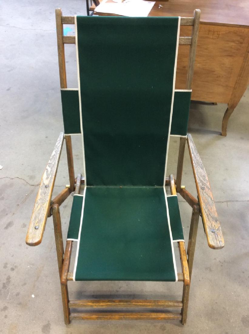 Folding Wooden and Canvas Armchair: Folding wooden arm chair contains green toned fabric with white lining. Chair is designed with a straight back. Contains weathering. Measures approx 39 inches tall x 24.5 inches wide x 32 inches deep.