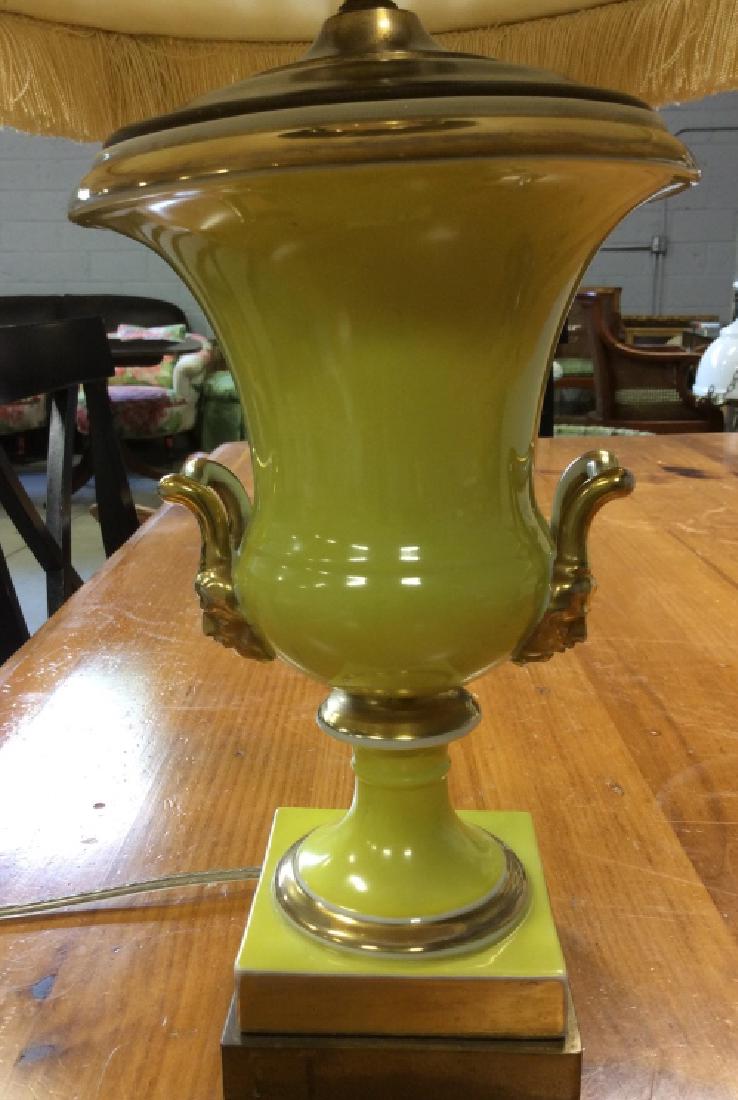 Metal Lemon Yellow Trophy Table Lamp: Metal trophy table lamp contains lemon yellow tone with gold toned handles with faces. Base is square and gold toned. Lamp shade is cream toned with ruffles and fringes. Contains minor discoloring. Me