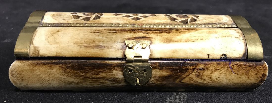 Bone & Brass Keepsake Box: Bone & brass keepsake box is tan toned. Lid of box contains carved out designs in various shapes. Brass is on the hinges and along the edge of the lid. Inside the box is purple toned fabric with minor