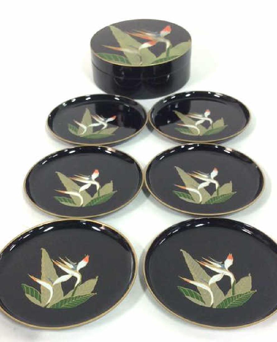 Lacquerware Set Of Coasters: Set of 6 Bird Of Paradise Japanese coasters are black toned and concealed in a cylinder designed with birds and a plant. Coasters contain gold toned rims along the edge. Measure approx 4 inches in dia