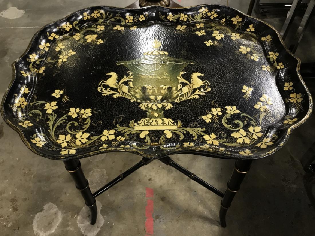 Black & Gold Toned Ornately Detailed Tray Table: Table top contains gold and olive toned ornate floral, leaf, grape and vine motif detail. Has evident paint cracking. Contains 4 legs. Measures approx 19 inches tall 22 inches long 16 inches deep. Pie