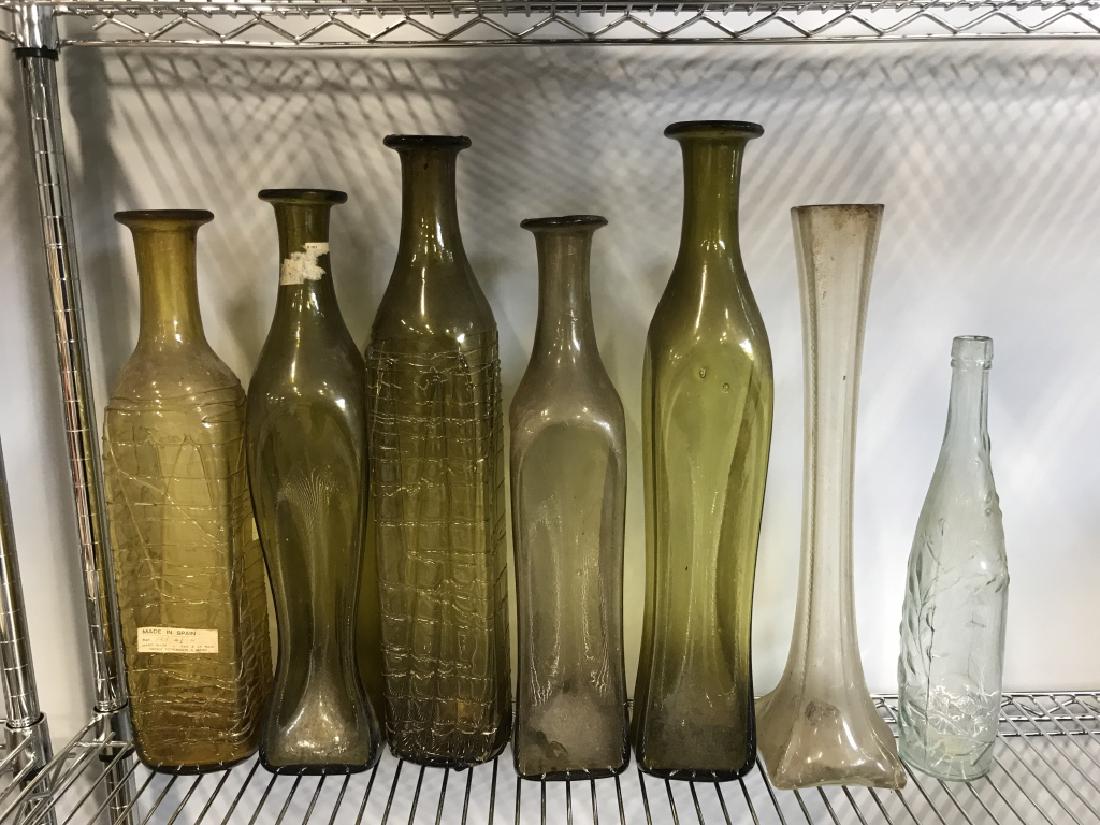 Lot 7 Art Glass Bottles Made In Spain: Includes 5 green toned bottles and 2 clear bottles. Some are labeled Made in Spain. Largest piece measures approx 20 inches tall 4 inches wide. Need cleaning. Property of Bedford New York Estate, and 