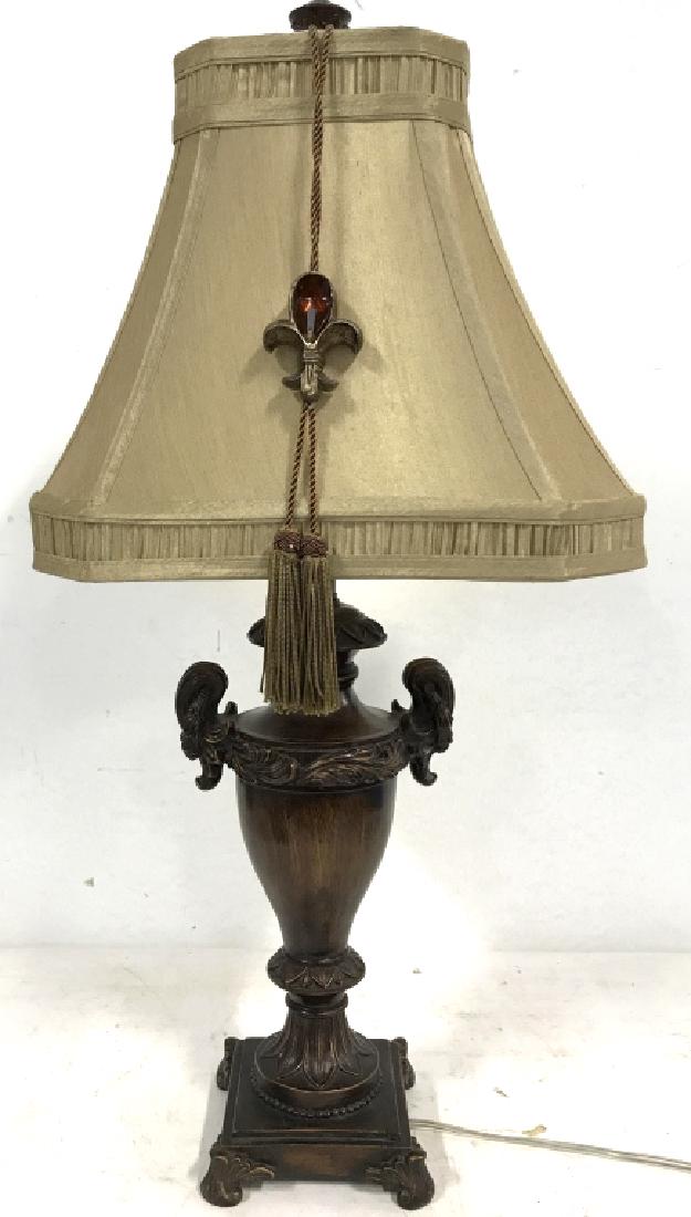 Carved Wooden W Shade & Finial: Lamp has carved wooden detail. Shape resembles a trophy. Some carved detail is ornate. Has 4 carved wooden feet. Shade is gold toned while lamp is brown toned. Has small tassel like detail tied around
