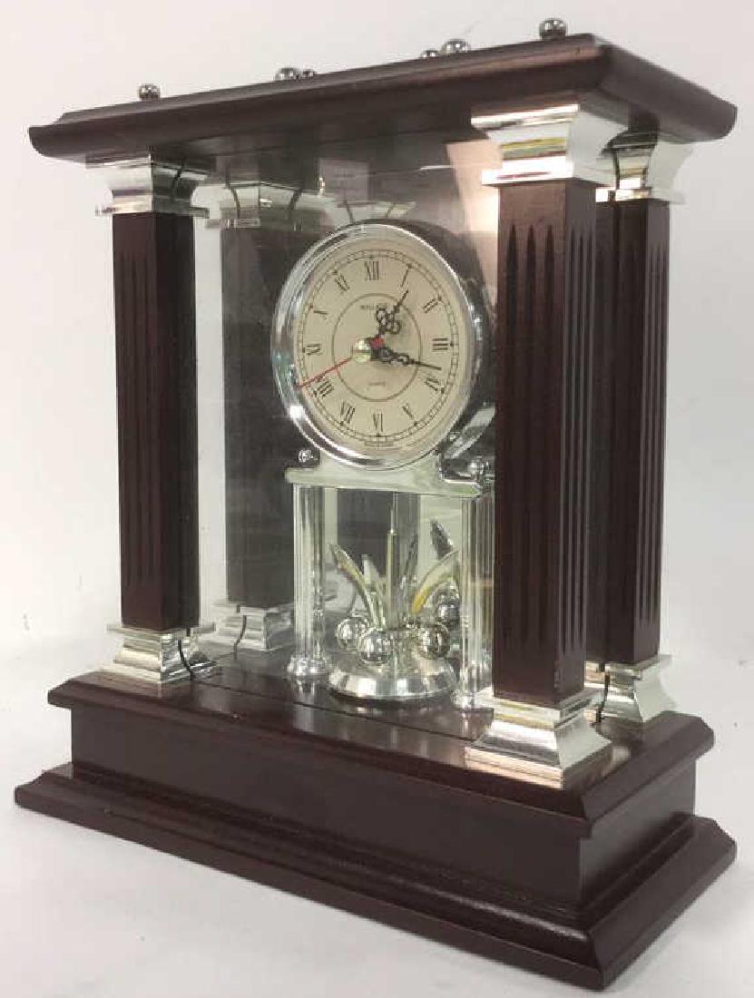 WALLACE SILVERSMITHS Wooden Desk Clock: Label on underside reads WALLACE SILVERSMITHS. Has a dark brown maroon tone. Interior has silver toned elements and cream toned clock face with black toned roman numerals. Measures approx 10 inches ta