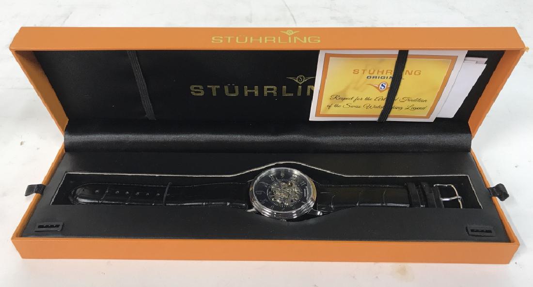 STUHRLING Watch In Original Box: Watchface reads STUHRLING ORIGINAL. Watch band is possibly leather. Watch measures 10 inches long when fully extended. Box is orange toned and outer covering is black toned. Includes instruction manua