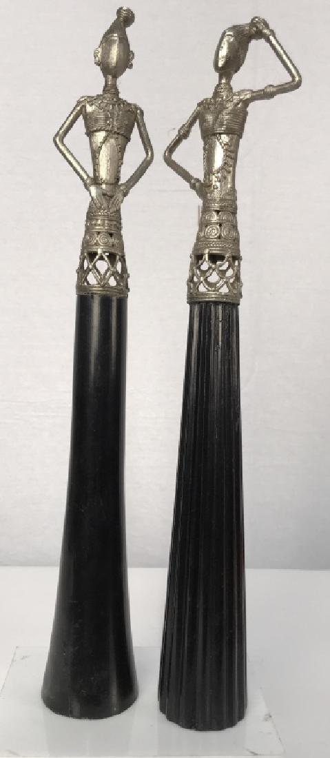 Decorative Ebonized Wood and Metal figurals: Decorative Ebonized Wood and Metal figurals of two women, dressed in tribal style attire affixed to elongated ebonized wood pedestals, each measures 3 in diameter of base x 21 in to top of headdress, 