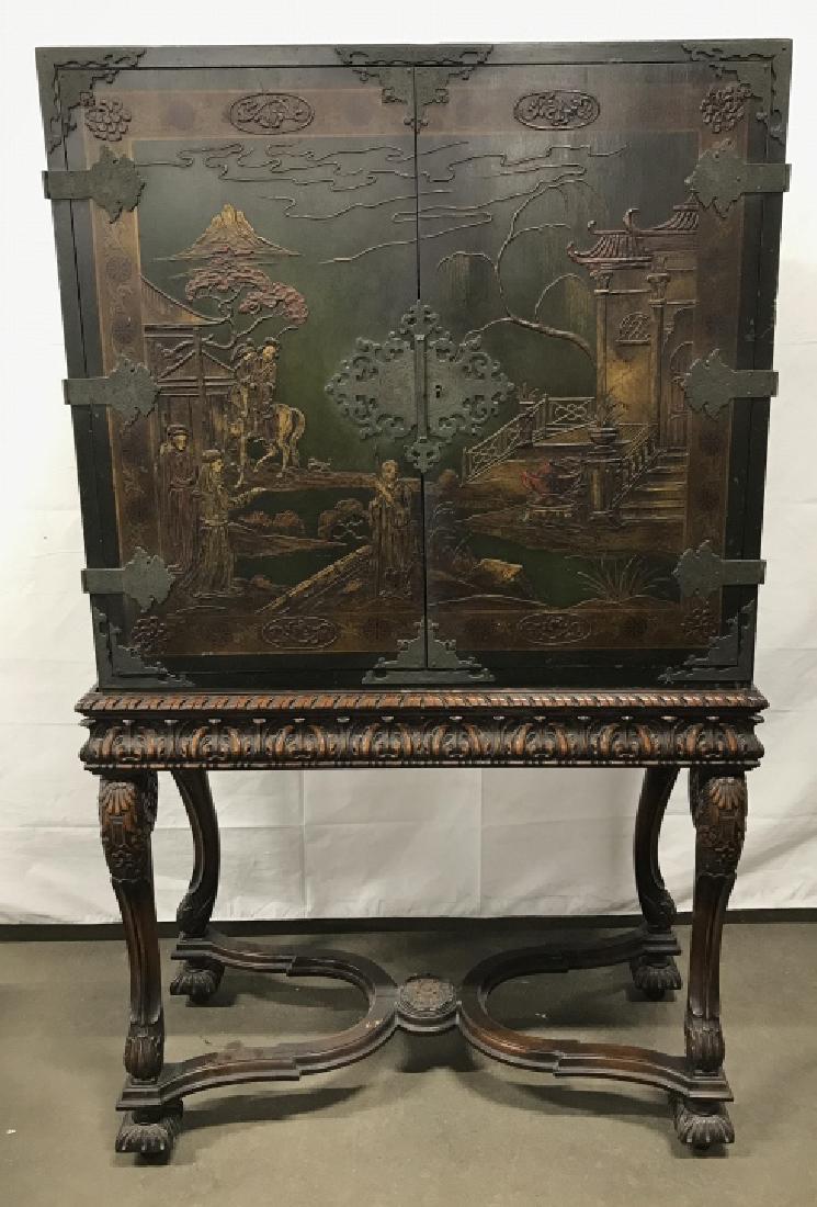 Carved Wooden Oriental Cabinet On Base: Carved Wooden Oriental Cabinet with hand painted Chinoiserie scenery over dark green and black base. Cabinet doors have etched metal hinges and center medallion with intricate design that open to two 