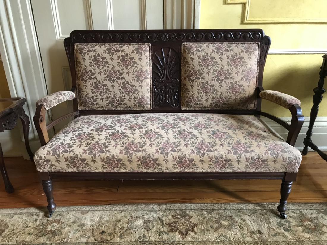 Hand Carved & Upholstered Double Chair Back Settee: Vintage poss antique dark toned wooden Double Chair Back Settee with hand carved leaf and scroll motif at center of back, turned front legs on casters, pink, green and beige toned Upholstered seats, b