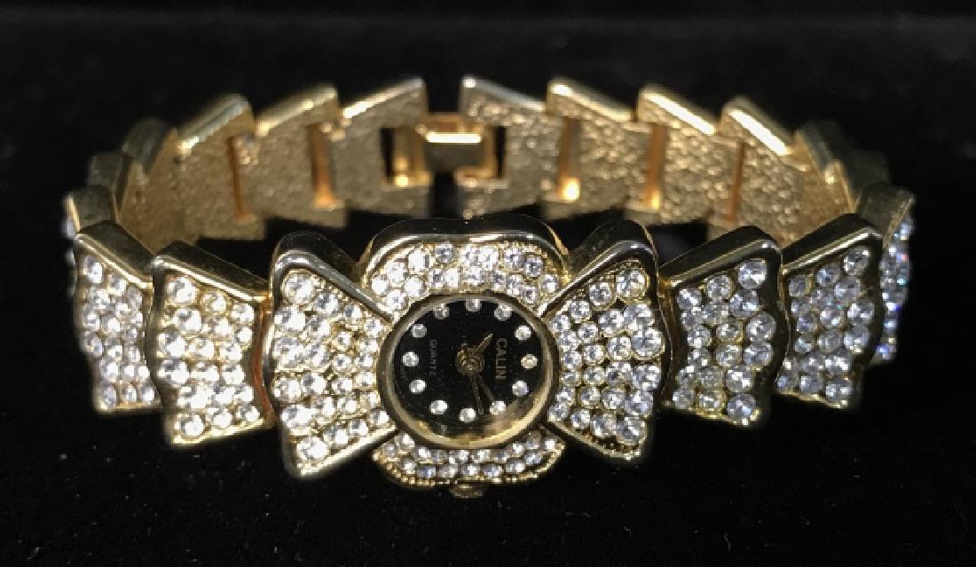 Calin Quartz Rhinestone Ladies Wrist Watch: A Calin Quartz ladies wrist watch with gold toned metal base and band with a multitude of small rhinestones, and a black face with small rhinestones marking the hours. Marked Calin Quartz on face. Mea