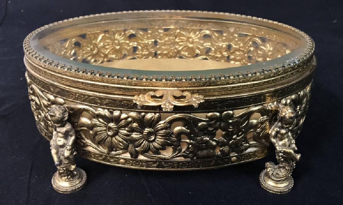 Oval Gilt Metal Floral Pierced Jewelry Box: Vintage/Antique Jewelry Vanity Trinket Box Ormolu Case with floral pierced filigree, Cherub Feet, beveled clear glass top, and velvet interior. Measures approx 8.25 inches long x 7 inches wide x 3.25 