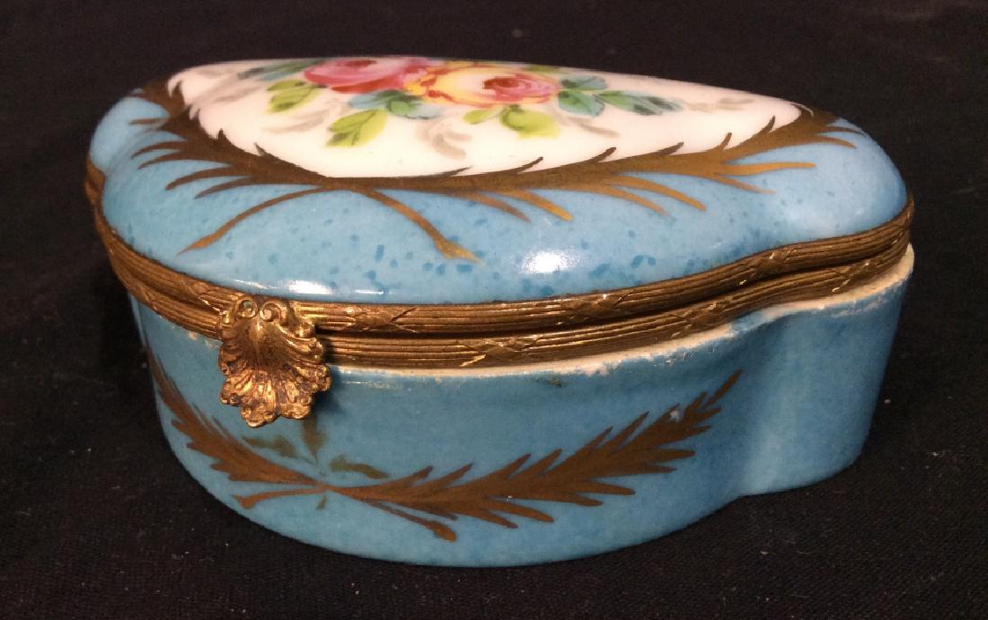 Porcelain Bronze Mounted Trinket Box: Porcelain Bronze Mounted Trinket Box, 1 1/2 in x 6 in, Lidded, with Shell form closure, bronze edges reeded and crosshatches, good condition, unmarked, blue on white ground with painted floral design 