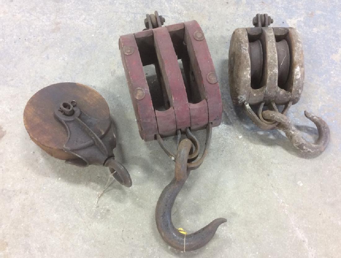 Group of 3 Vintage Wheel Farm Pulley Tools: Group of 3 Vintage, possibly antique, wheel farm pulley tools. Two tools have hooks on the ends. Largest pulley Approximately 19 inches in length with hook, 6 inches in height. Metal and wood. Vintage