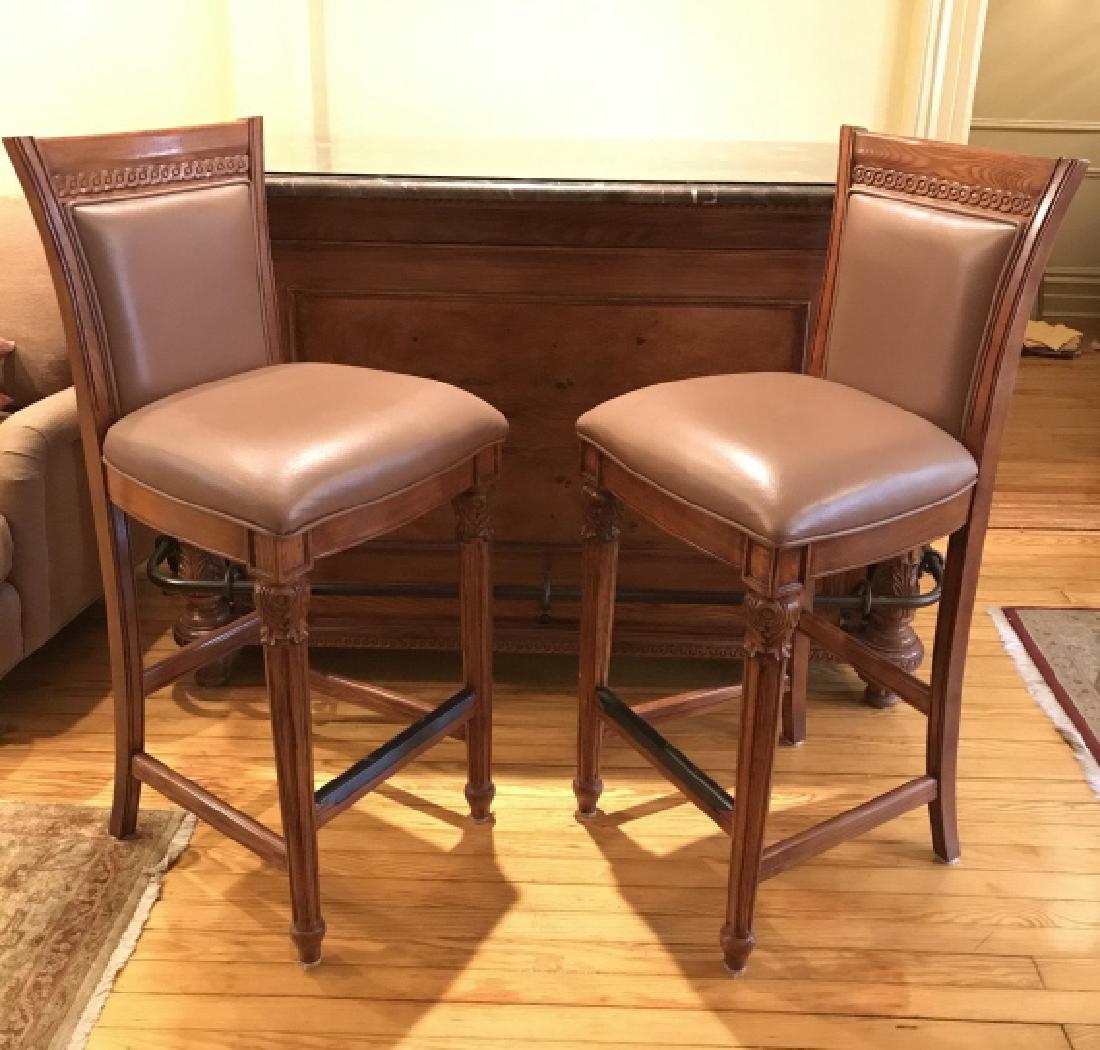 Pair Carved Wooden Bar Stools W Upholstered Seat: Pair of carved wooden bar stools with column front legs and faux leather Upholstered seats and backs. No condition issues noted. Bar Stools. Wooden Home Bar. Holiday entertaining. Man Cave Accessory. 