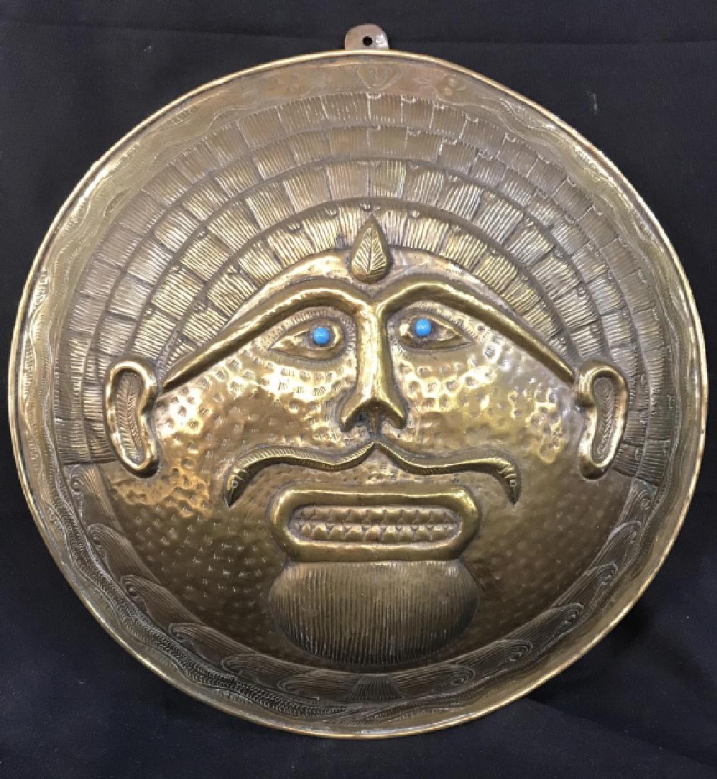 Gold Toned Repousse Brass Shield Wall Decor: Shield wall decor has beveled depiction of face with blue toned eyes. Appears to possibly be Asian. Piece is vintage possibly antique. Measures approx 13 inches diameter. Asian arts and crafts, orient