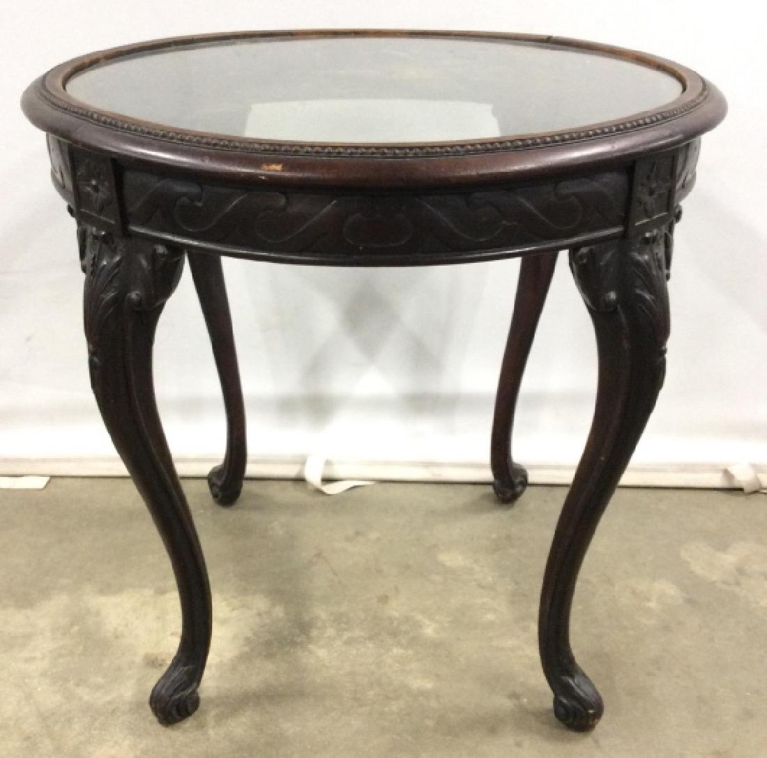 Vintage Carved Wooden Glass Top Table: Table has carved wooden detail. Contains 4 legs with carved wooden feet. Table has glass top. Measures approx 24 inches tall and diameter. End table, side table, lamp table, cabriole legs 6.