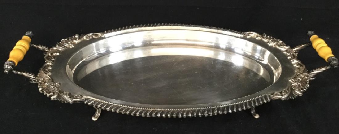 Silver Toned Footed Serving Tray W Handles: Underside appears to be marked ES with image of crown. Piece is silver toned with ornate detail at sides. Handles appear to possibly be Bakelite. Piece is footed. Measures approx 24 inches long 12.5 i