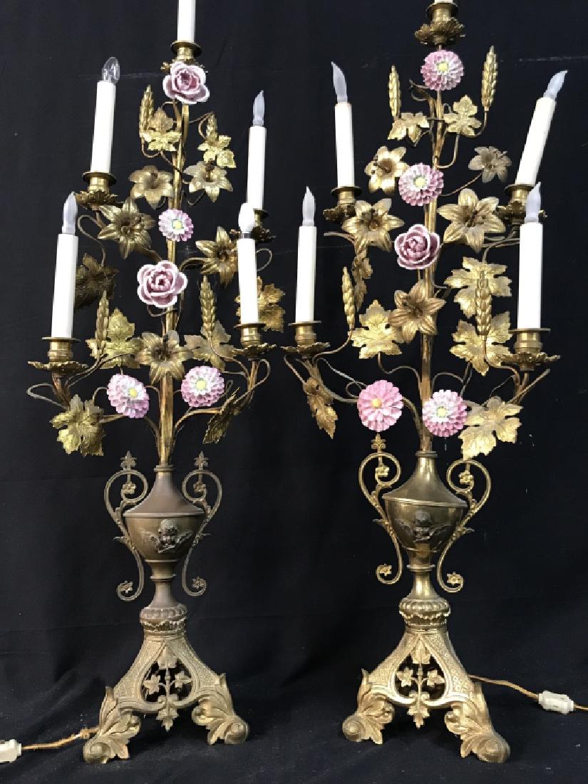 Pair Extravagant Brass Lamps W Porcelain Flowers: Extravagant brass table lamps with Capodimonte style porcelain flowers. Each lamp has 5 arms w candle bulbs. Three feet base leads to cherub angel adorned urn body, which extends out to brass metal fl