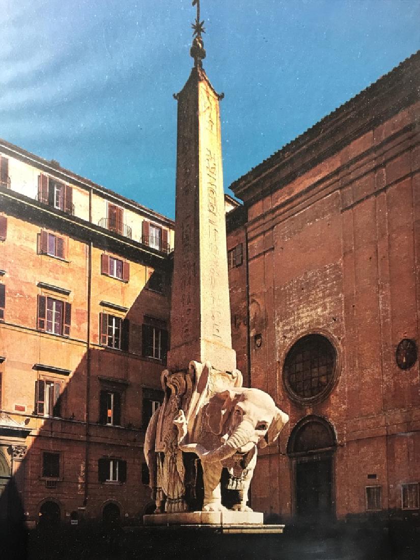 Framed Print of Elephant and Obelisk: Framed print of Elephant and Obelisk in Rome. Print is possibly a magazine page. Print is in painted wood frame with gold tone trim. Frame has surface wear. Measures approx 13.75 inches in height by 1