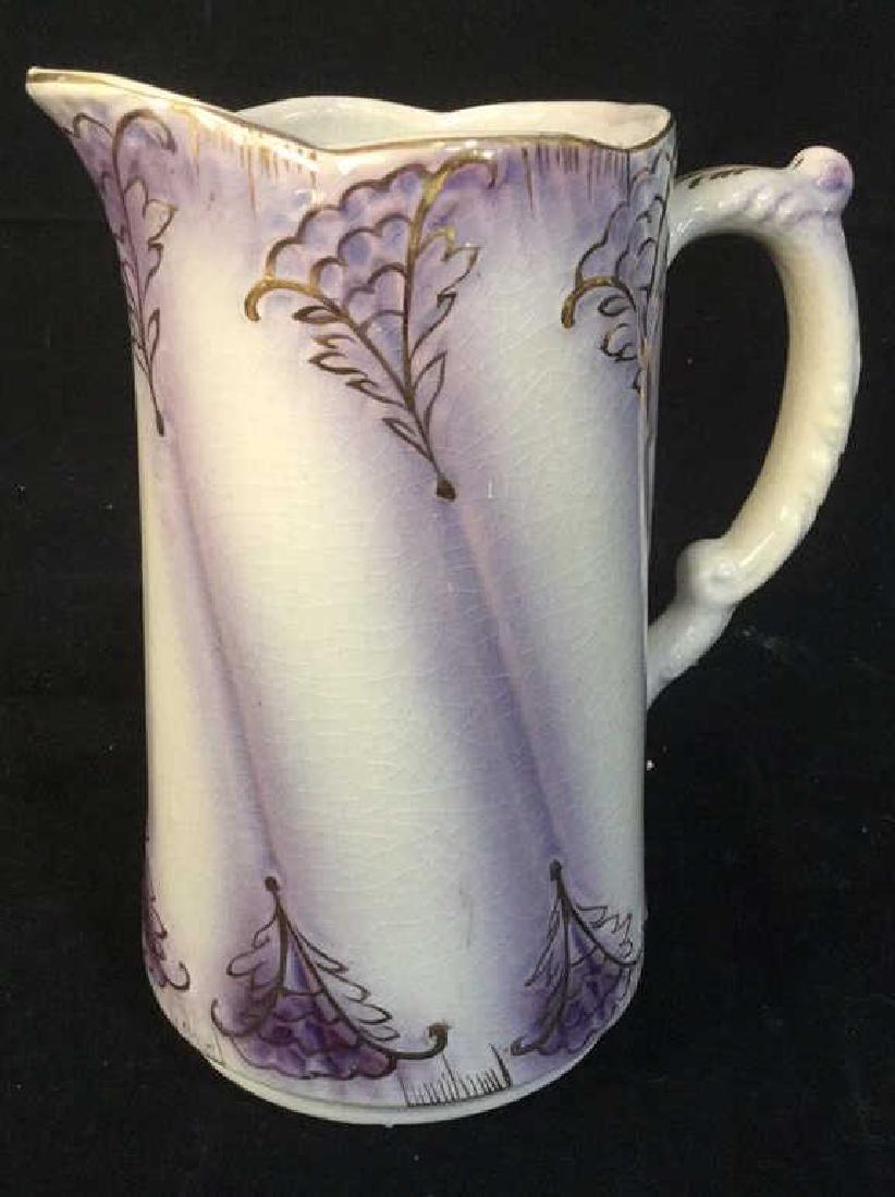 Signed Porcelain Pitcher: Cream toned porcelain with purple toned accents, gold toned painted trim and floral design, evident crazing, signed illegibly on underside. Measures approx 7in by 6 in By 4 in. Tableware, tabletop acc