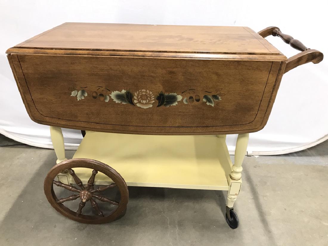Carved Wooden Drop Leaf Beverage Cart: Cart is wooden. Contains 2 small black toned wheels & 2 large carved wooden wheels. Cart has drop leaf on each side. Has tones of yellow & light brown with painted floral & leaf detail. Measures appro