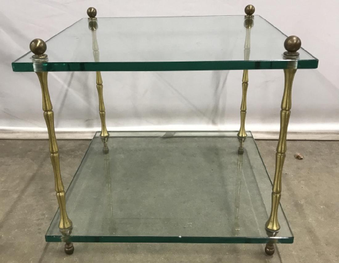 Two Tiered Glass And Metal Side Table: Two Tiered Glass And Metal Side Table, two square glass shelves connected by four brass toned legs, measures approximately 16 inches tall x 18 inches square, some surface scratches to glass and one ni