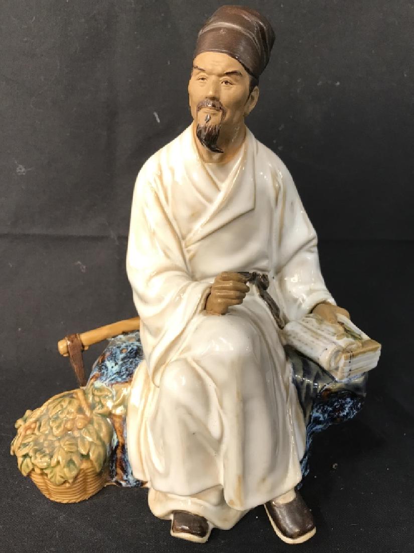 Ceramic Porcelain Seated Male Figure: Figure depicts a seated male figure holding a book with an axe behind him. Piece measures approx 9 inches tall 7 inches wide, 5 inches deep. Porcelain sculpture, art sculpture, tabletop accessory, hom