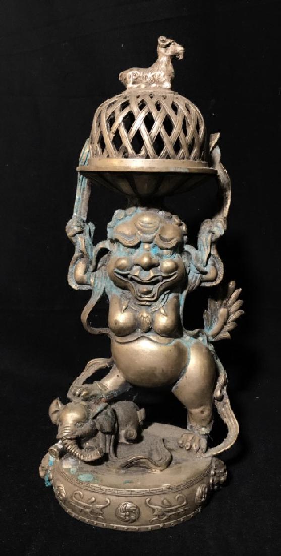 Chinese Buddhist Tantric Incense Burner Smoker: Chinese Buddhist Tantric Incense Burner Smoker depicting a deity stepping on an elephant and holding tray with goat topped lid, shows signs of patina to metal, measures approx 13.5 inches tall x 6.5 i