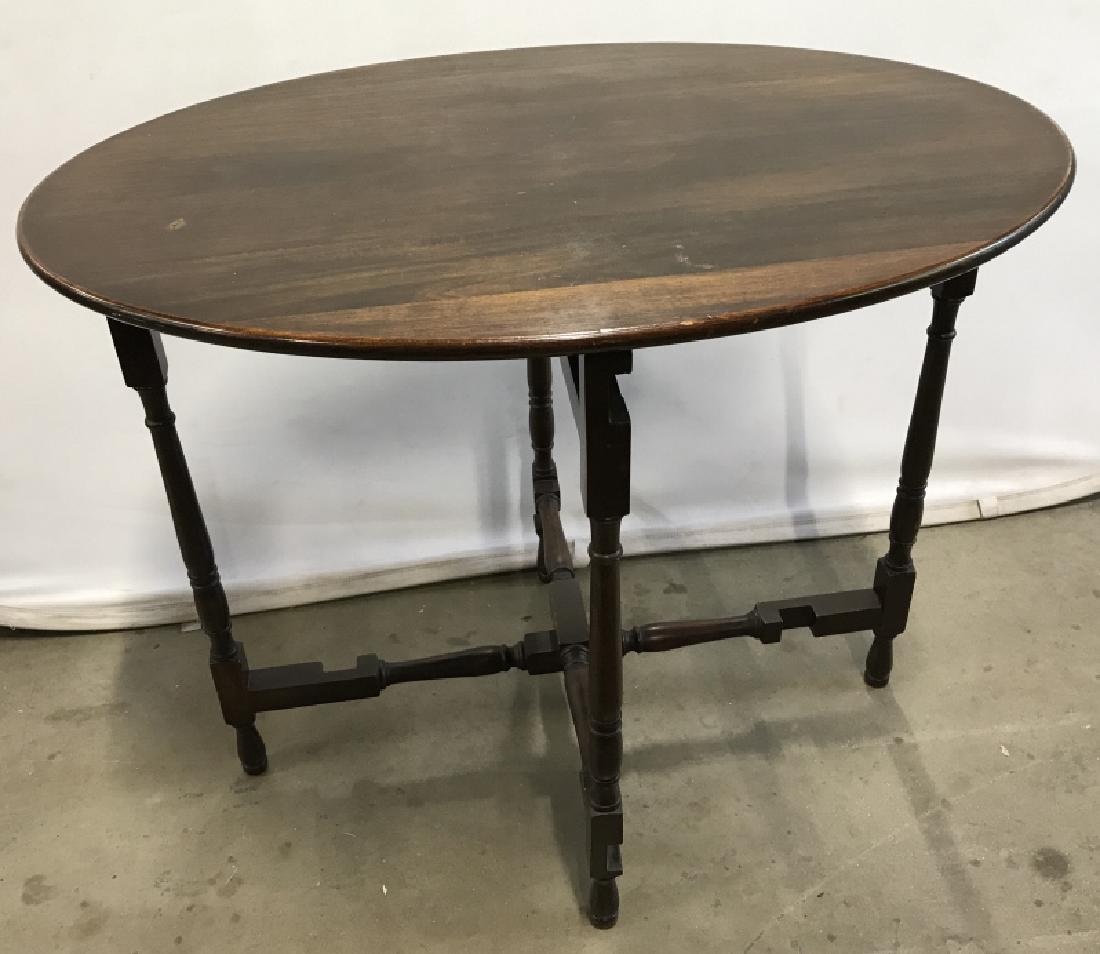 Vintage Drop Leaf Side Table With Turned Legs: Vintage Dark Toned Wooden Side Table With Turned Legs, oval in shape, legs pivot so top drops down for easy storage, some surface marks and scratches due to age and use, measures approx 34 inches wide