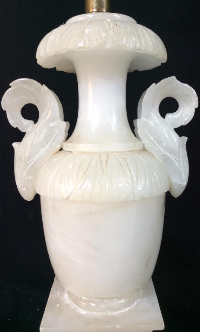 Carved Stone Urn Table Lamp: Carved stone, possibly Alabaster, is white in tone. Lamp has brass stem. Lamp has not been tested. Measures approx 28 inches in height by 7 inches in width with side handles, 5.25 inches in depth. Som