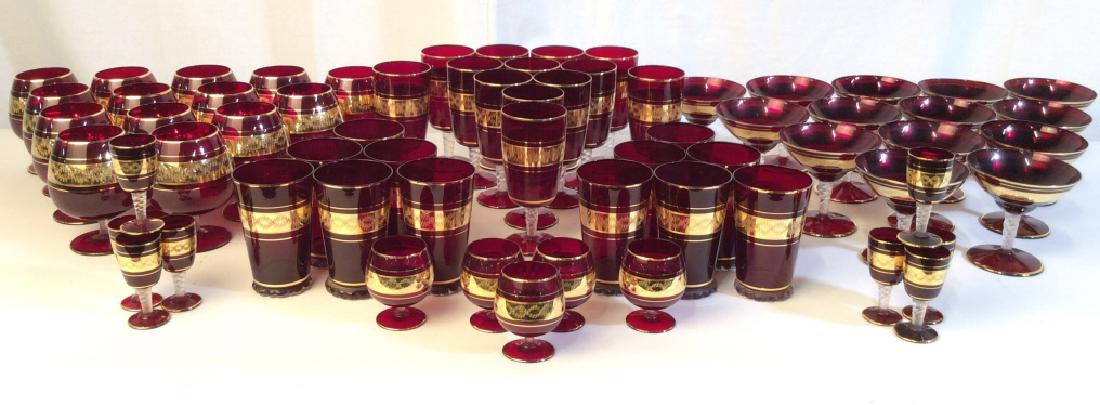 Lot 64Cranberry & Gold Toned Bohemian Glass Set: Lot includes 14 cocktail glasses, 12 Brandy snifter glasses, 5 wide set cordials, 8 tall cordials, 12 highball glasses, & 13 tall wine glasses. Pieces appear to be crystal. Pieces are cranberry and go