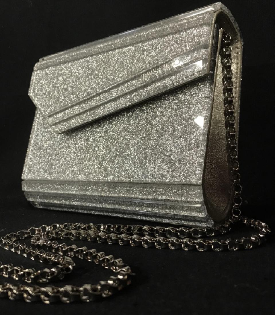 JIMMY CHOO Silver Acrylic Glitter Evening Clutch: Structured Evening clutch has glitter acrylic outer shell, marked for JIMMY CHOO. Snap closure. Interior is lined with champagne tone satin style fabric, with interior pocket marked for JIMMY CHOO. Ha