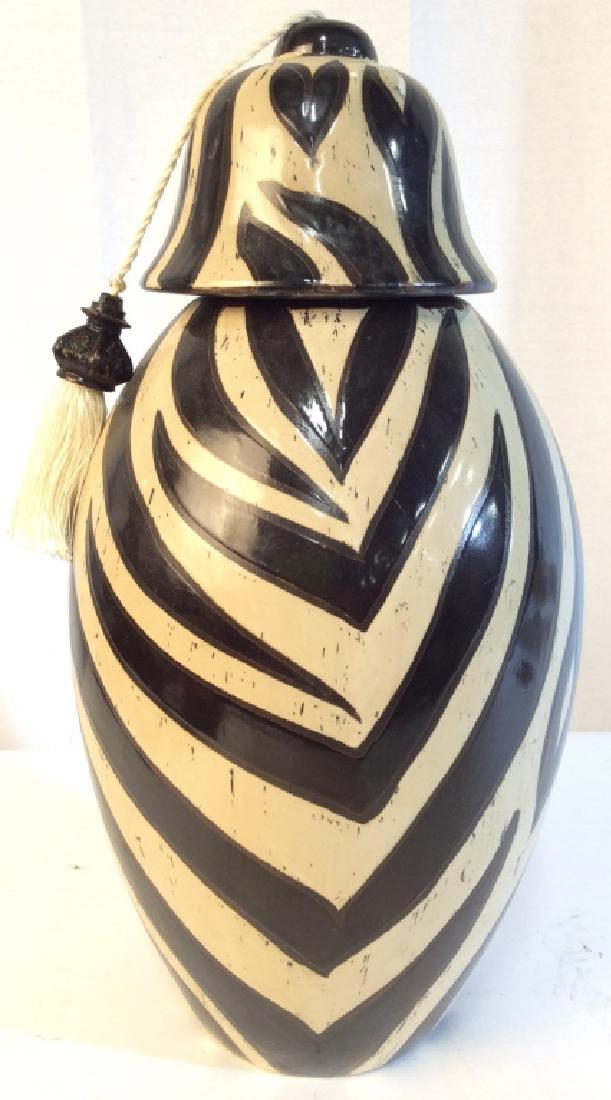 Zebra Style Lidded Porcelain Urn: Piece has black & cream toned detail. Piece is porcelain. Urn includes lid with tassel. Piece measures approx 18 inches tall 9 inches wide. Rim has noticeable chip. shelf piece, home accent, urn, vase