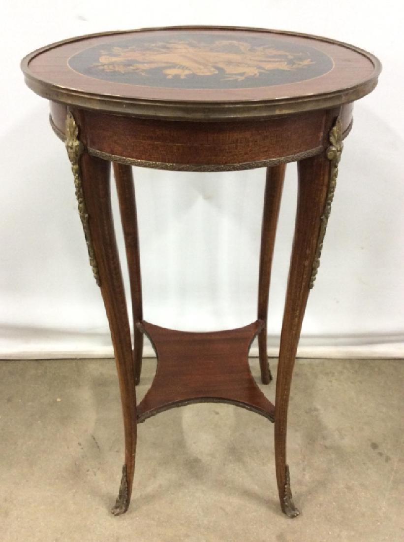 Vintage Round Wooden Side Table: Top of table has depictions of various instruments with floral vine and leaf detail. Table top is round. Edge of table top has dark toned toned metal accent. Legs have gold toned metal detail. Measure