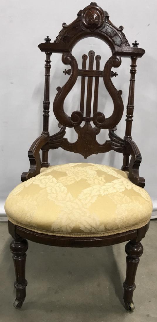 Vintage Carved Wooden Chair W Casters: Chair is wooden. harp back design, Contains intricately carved wooden detail. Cushion of piece is gold toned with leaf detail. Front 2 legs of piece is on casters. Measures approx 41 inches tall 24 in