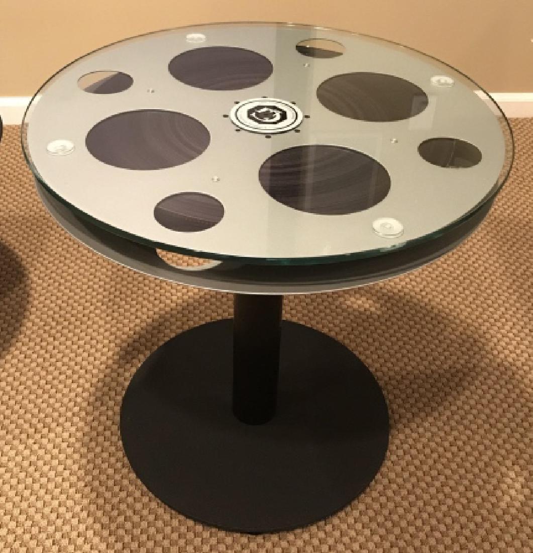 Pair Glass Top Film Reel Side Tables: Side tables are stylized as film reels atop pedestal bases, with glass tops. Tops of film reels are marked for Goldberg Brothers. Each measures approx 23.5 inches in height by 24.5 inches in diameter.