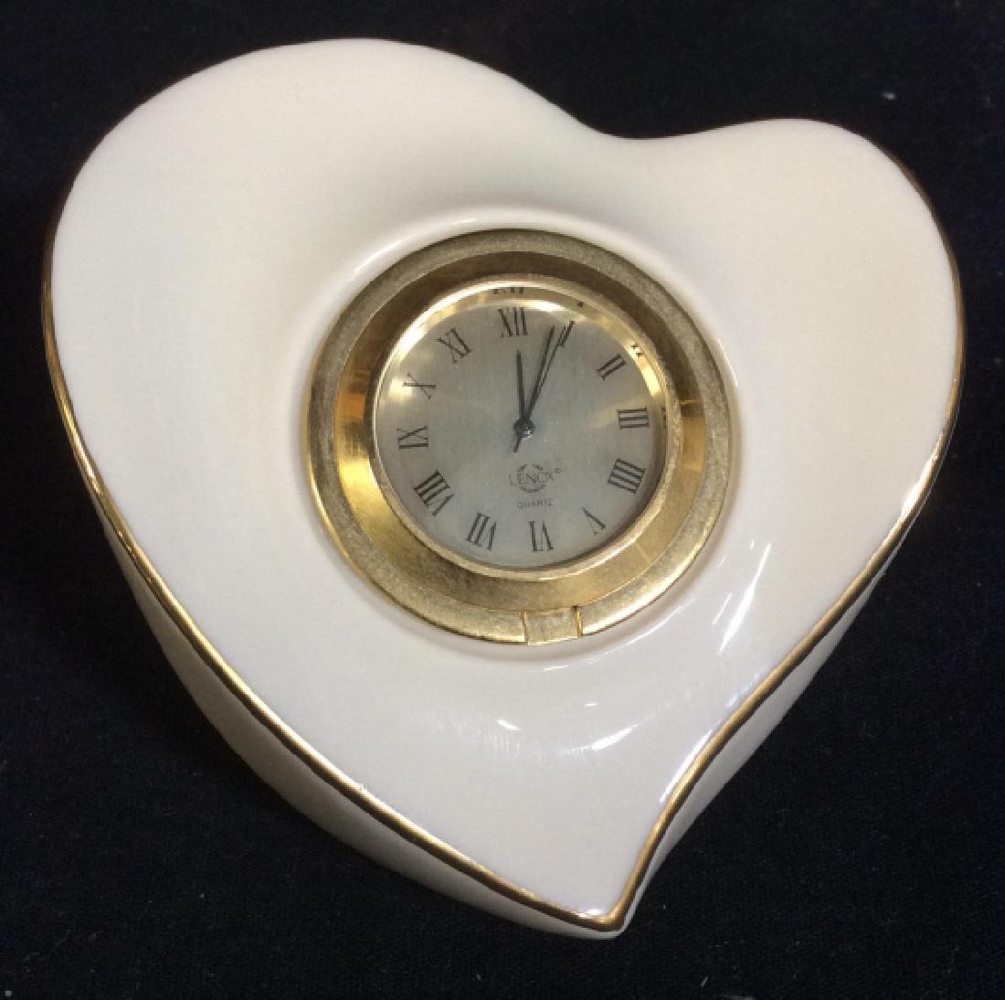 LENOX Porcelain Heart Shaped Clock: Underside of piece is marked LENOX. Piece is cream toned with gold toned accents. Clock Face is gold toned with black toned Roman numerals. Measures approx 3.5 inches wide, 2.5 inches tall. clock, tab