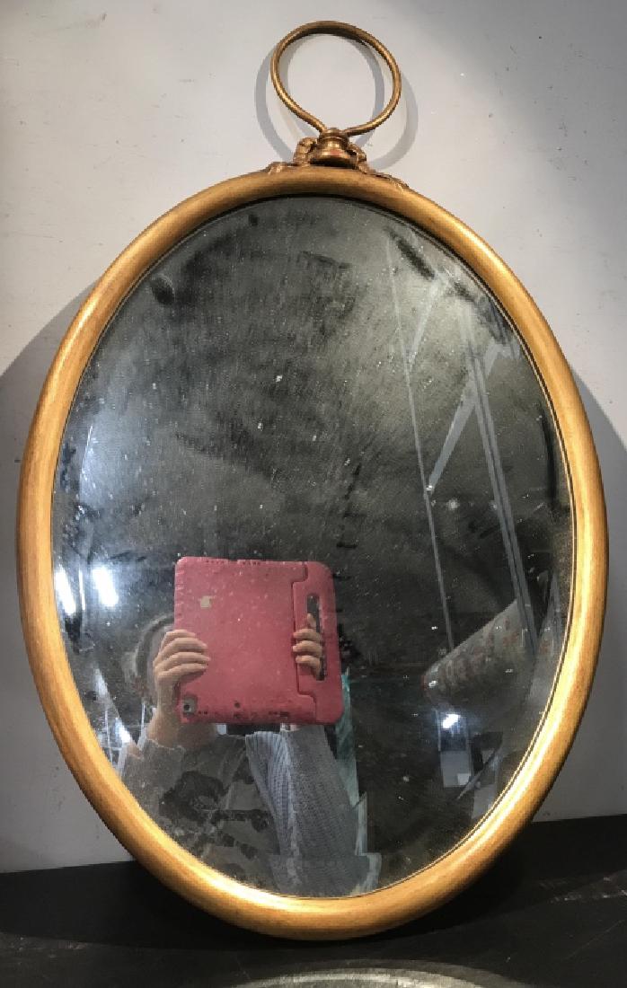 Beveled Oval Mirror in Gold Tone Wood Frame: Frame has bell and loop hook detail on top. Measures approx 32 inches in height with upper loop, 19.25 inches in width. Some minor fading of gold tone on bell detail. Interior home decor, wall accent,