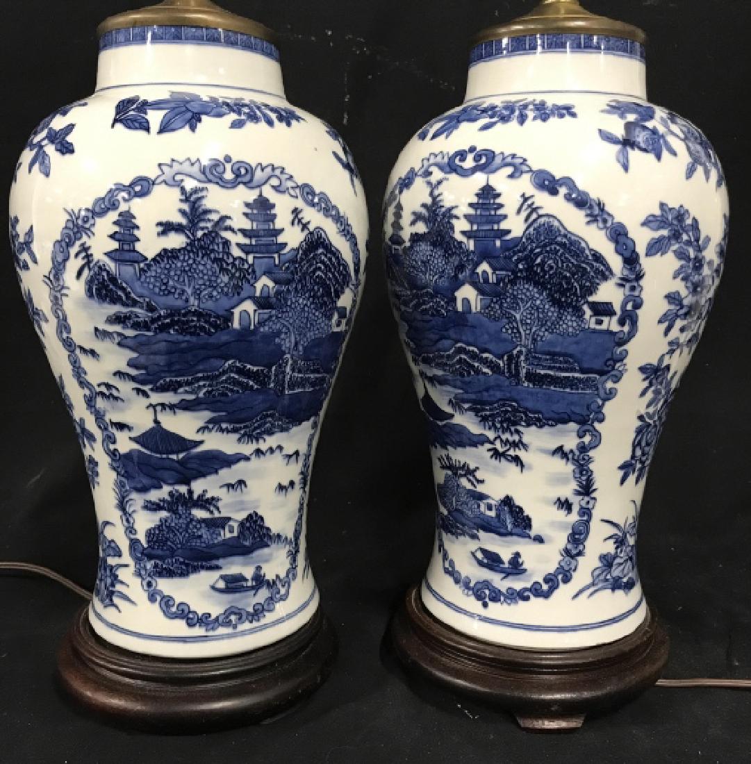 Pair Asian Blue & White Ceramic Table Lamps: Asian Blue & white ceramic table lamps with floral pattern surrounding buildings in landscape motif. Ceramic bodies sit atop wood bases. Each measures approx 26.5 inches in height including harp and f