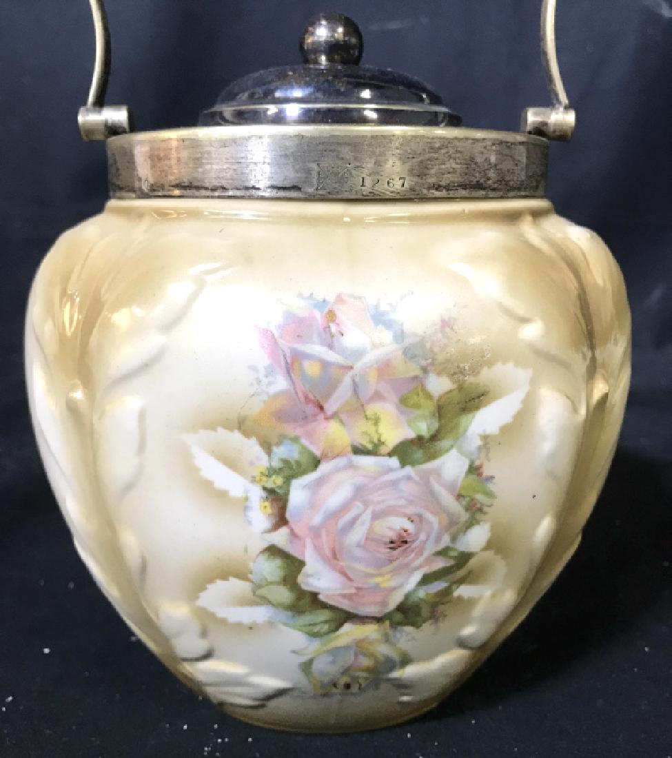 Lidded Porcelain Jar W Handle: Piece has tones of tan, white, pink, green, yellow, & light blue. Contains metal lid and handle. Piece measures approx 10 inches tall 6 inches wide. jar, ice bucket, tableware, tabletop accessory, tab