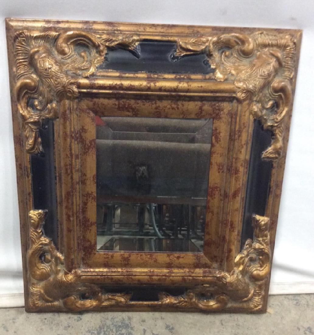 Beveled Mirror In 2-Tone Frame: Black and gold bronze tone material composite frame. Measures approx 20.5 inches in height by 18.5 inches in width. Setting of frame measures approx 9.5 inches by 7.5 inches. Interior home decor acces