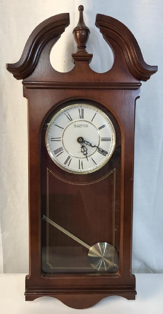 Carved Wooden HAMPTON Wall Clock: Piece has carved wooden detail. Piece reads HAMPTON on clockface. Clockface has black toned Roman numerals. Clock pendulum is gold toned, need re attachment. Measures approx 24 inches tall 11 inches w